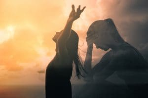 Eine Siluette einer Frau, die niedergeschlagen ist vor einem Sonnenuntergang.